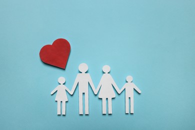Photo of Paper family figures and red heart on light blue background, flat lay. Insurance concept