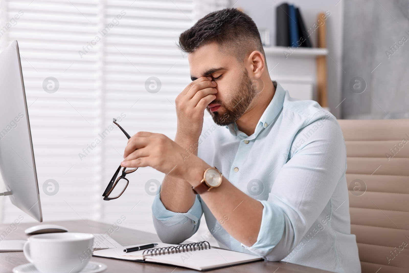 Photo of Overwhelmed man with glasses sitting at table in office