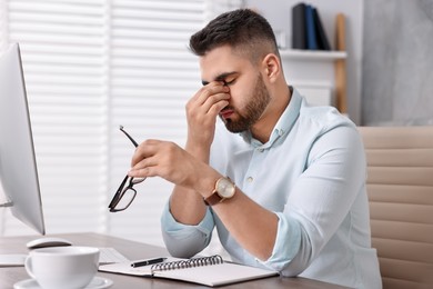 Photo of Overwhelmed man with glasses sitting at table in office