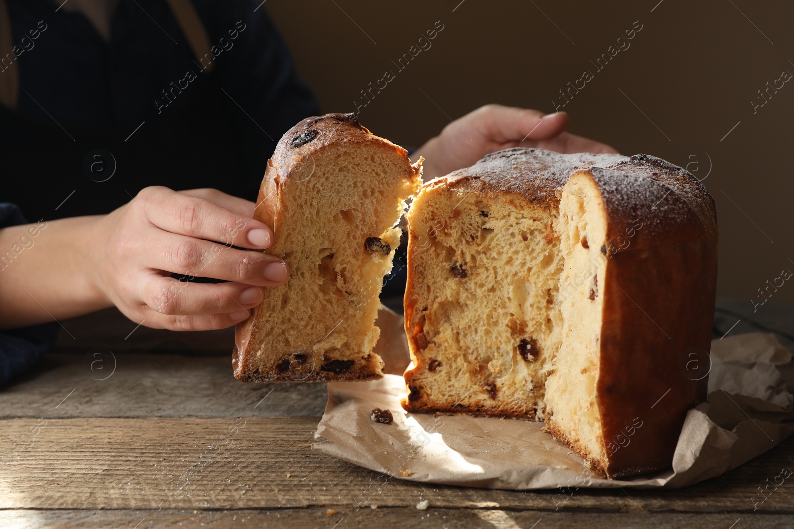 Photo of Woman taking slice of delicious Panettone cake with powdered sugar at wooden table, closeup. Traditional Italian pastry