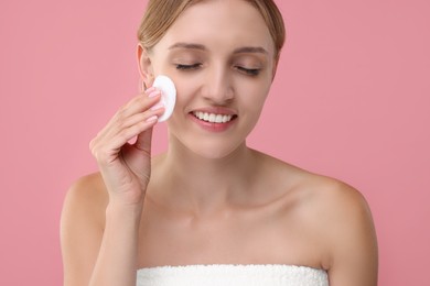 Photo of Young woman cleaning her face with cotton pad on pink background