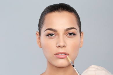 Photo of Young woman getting lips injection on grey background. Cosmetic surgery