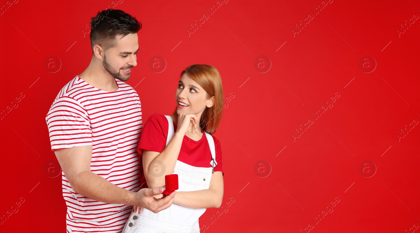 Photo of Man with engagement ring making marriage proposal to girlfriend on red background