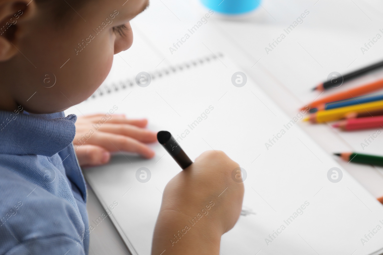 Photo of Little boy drawing with pencil at white table, closeup. Child`s art