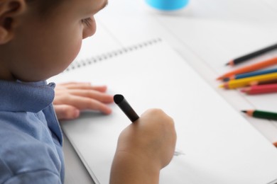 Photo of Little boy drawing with pencil at white table, closeup. Child`s art