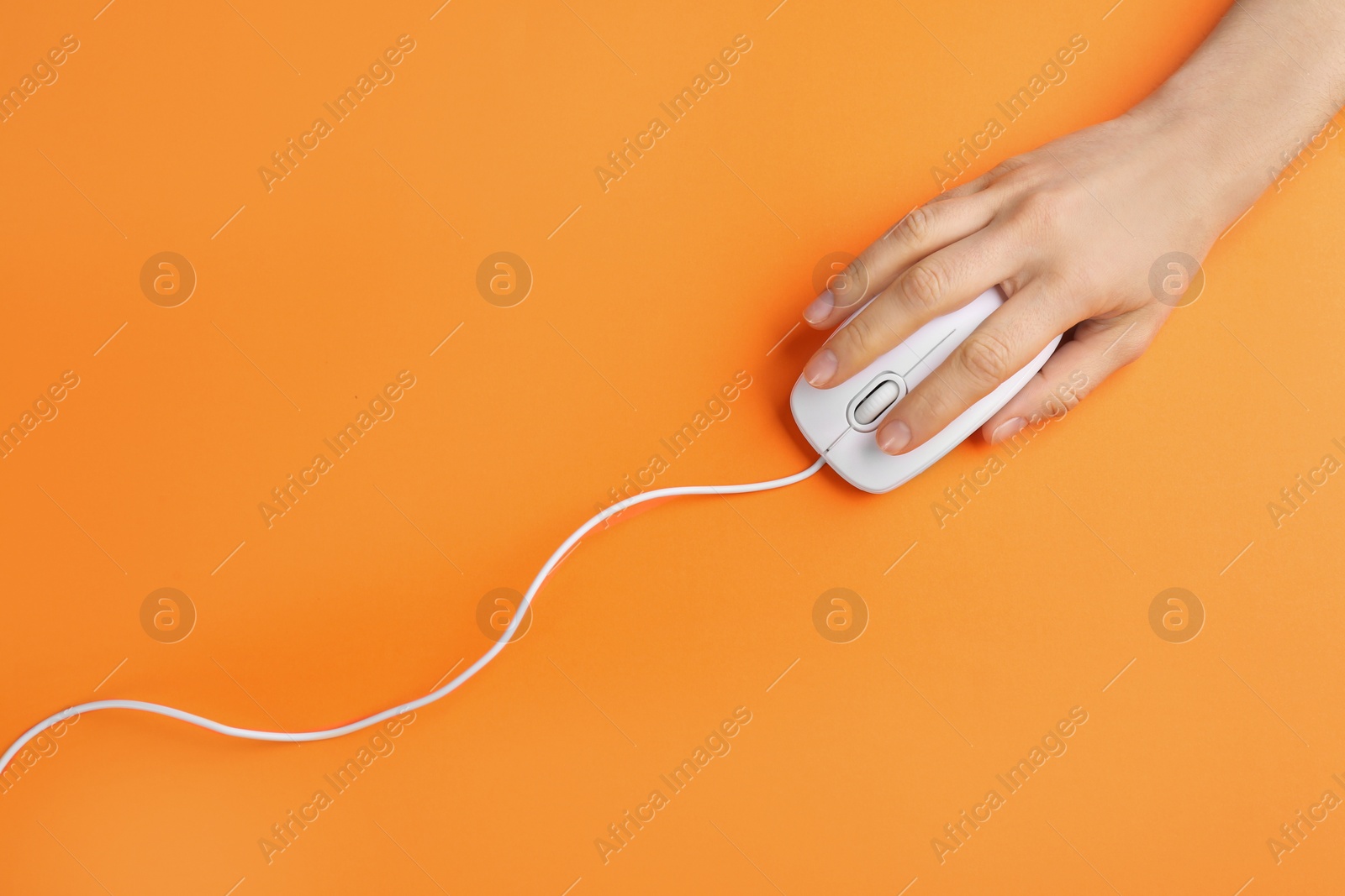 Photo of Woman using modern wired optical mouse on orange background, top view