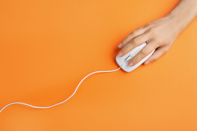 Photo of Woman using modern wired optical mouse on orange background, top view