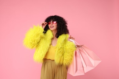 Happy young woman with shopping bags on pink background