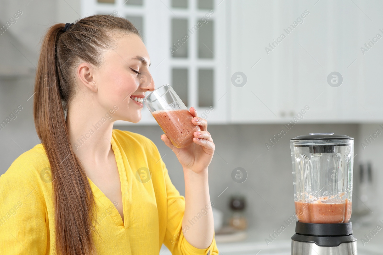 Photo of Beautiful young woman with delicious smoothie in kitchen. Space for text