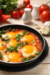 Delicious shakshuka in frying pan on light wooden table, closeup