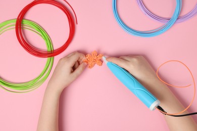 Boy drawing with stylish 3D pen on pink background, top view