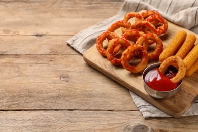 Photo of Tasty fried onion rings, cheese sticks and ketchup on wooden table, space for text