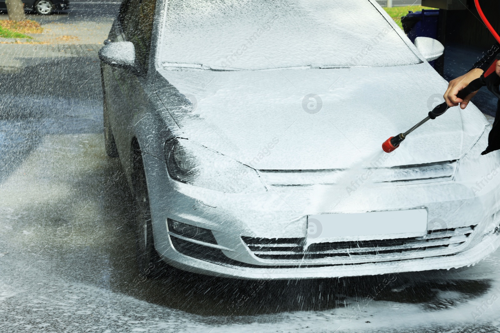 Photo of Man washing auto with high pressure water jet at outdoor car wash, closeup