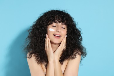 Beautiful young woman with sun protection cream on her face against light blue background