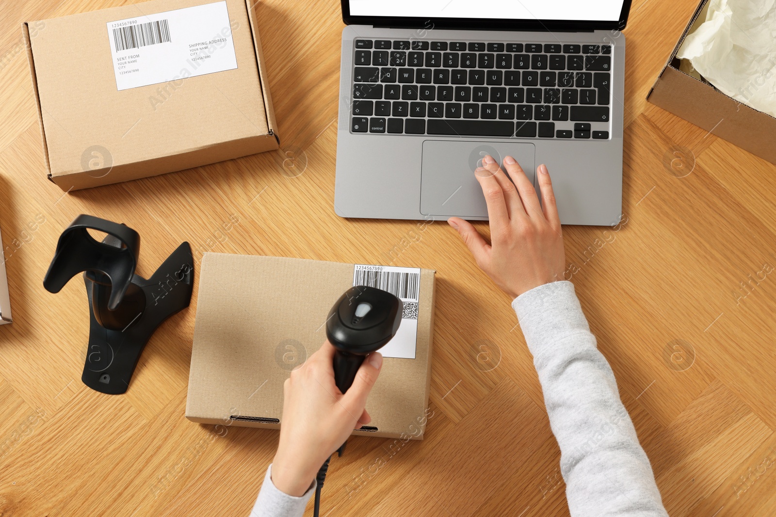 Photo of Woman with scanner reading parcel barcode at wooden table, top view. Online store