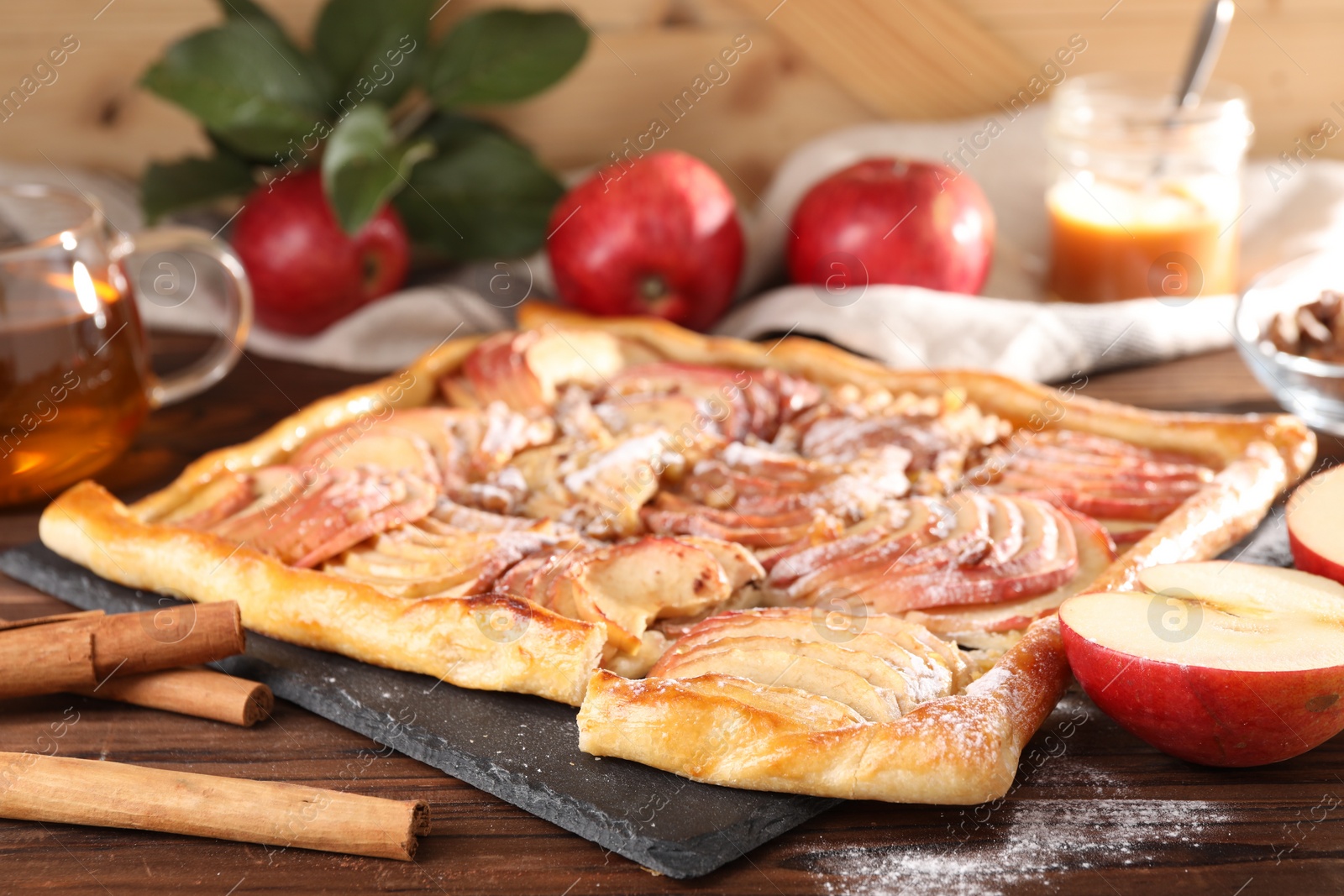 Photo of Tasty apple pie with powdered sugar, cinnamon sticks and fresh fruits on wooden table