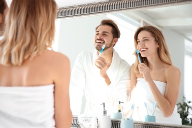 Photo of Young couple with toothbrushes near mirror in bathroom. Personal hygiene