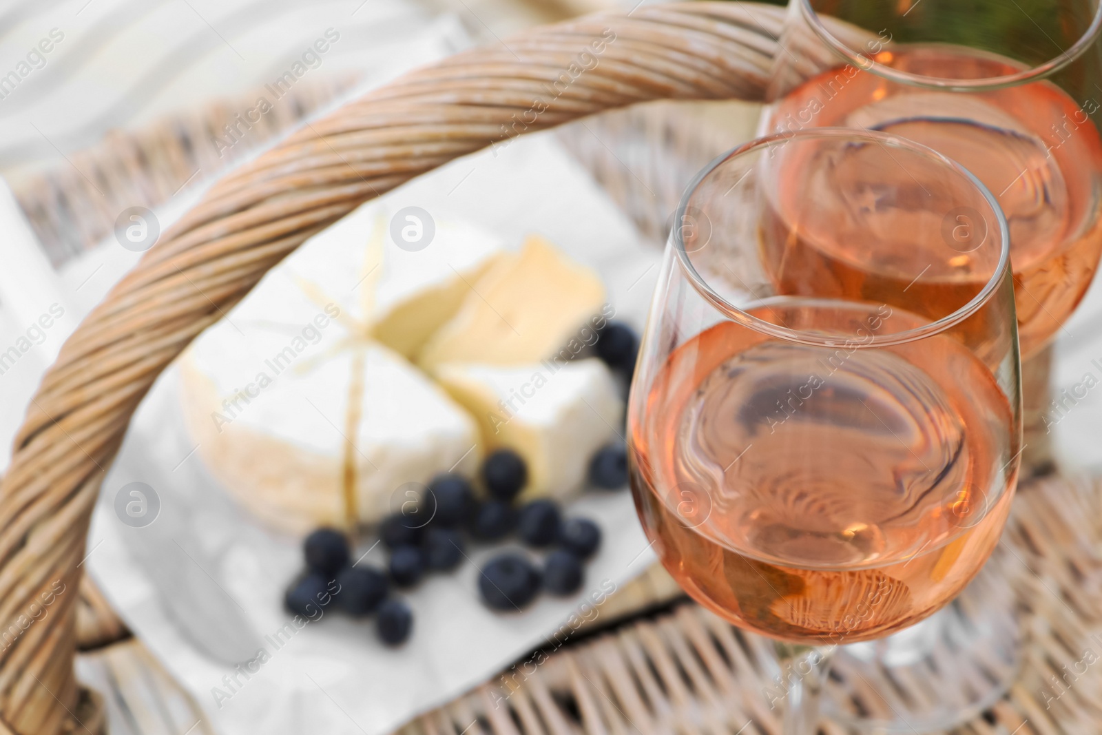 Photo of Glasses of delicious rose wine and food on picnic basket outdoors, closeup