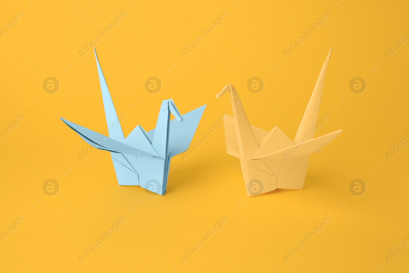 Photo of Origami art. Beautiful light blue and yellow paper cranes on orange background