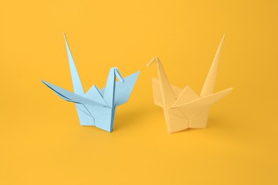 Origami art. Beautiful light blue and yellow paper cranes on orange background