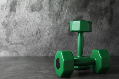 Photo of Green vinyl dumbbells on table against grey background. Space for text