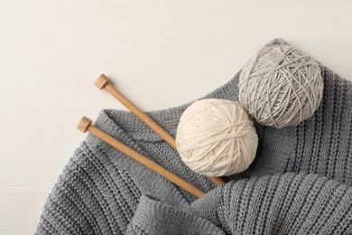 Photo of Woolen yarns, knitting needles and sweater on white wooden background, flat lay