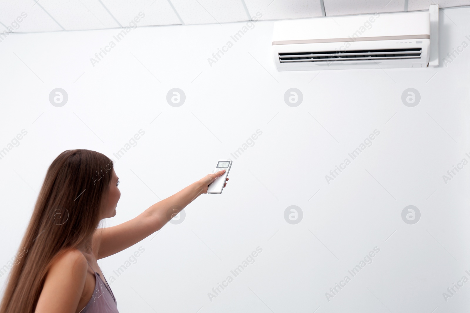 Photo of Woman operating air conditioner with remote control indoors