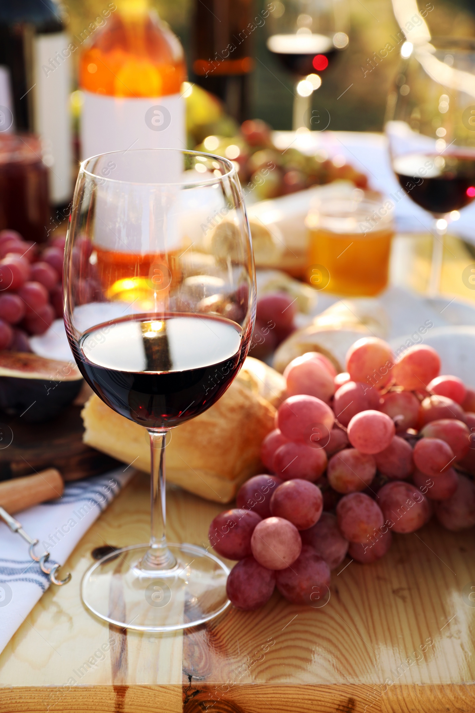 Photo of Red wine and snacks served for picnic on wooden table outdoors