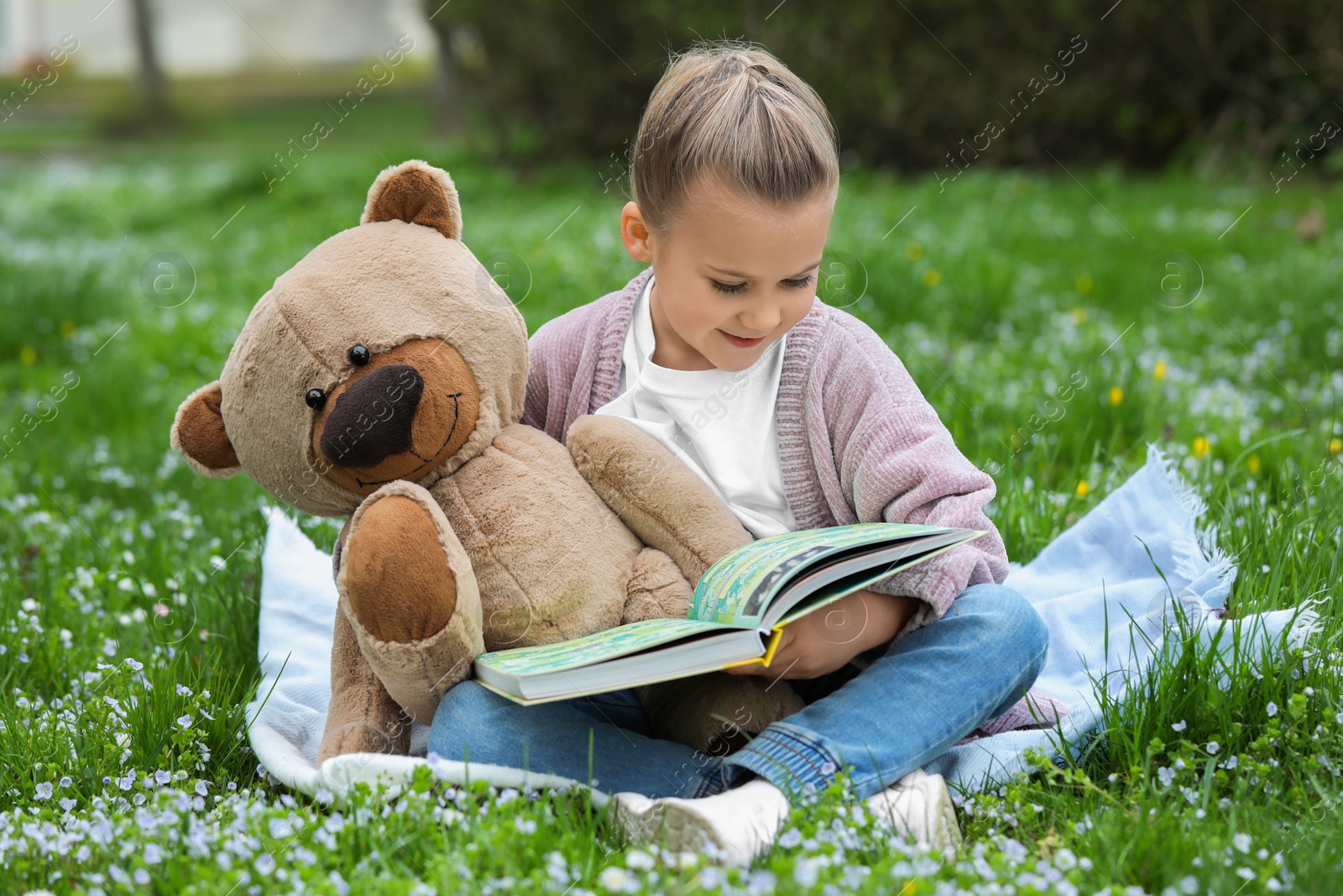 Photo of Little girl with teddy bear and book on plaid outdoors