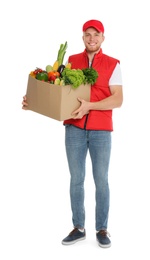 Delivery man with box of fresh vegetables on white background