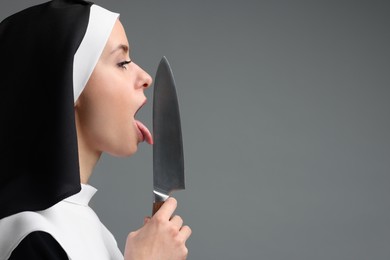 Photo of Woman in nun habit holding knife on grey background. Space for text