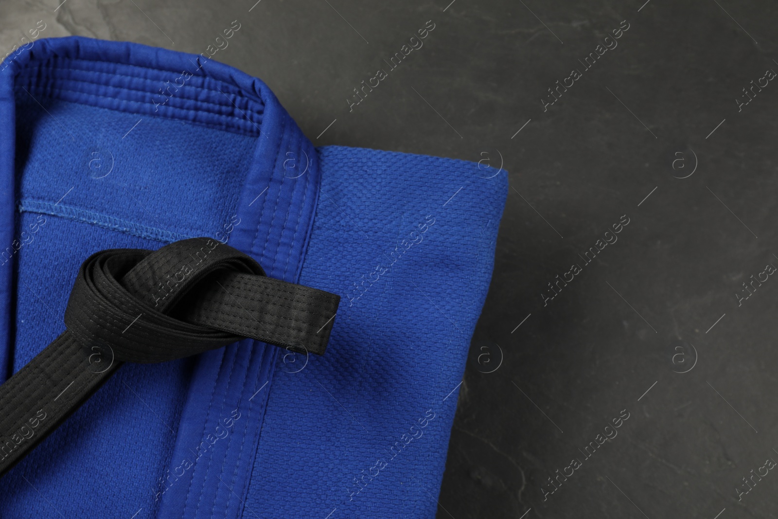 Photo of Black karate belt and blue kimono on gray background, top view. Space for text