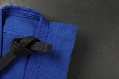 Black karate belt and blue kimono on gray background, top view. Space for text