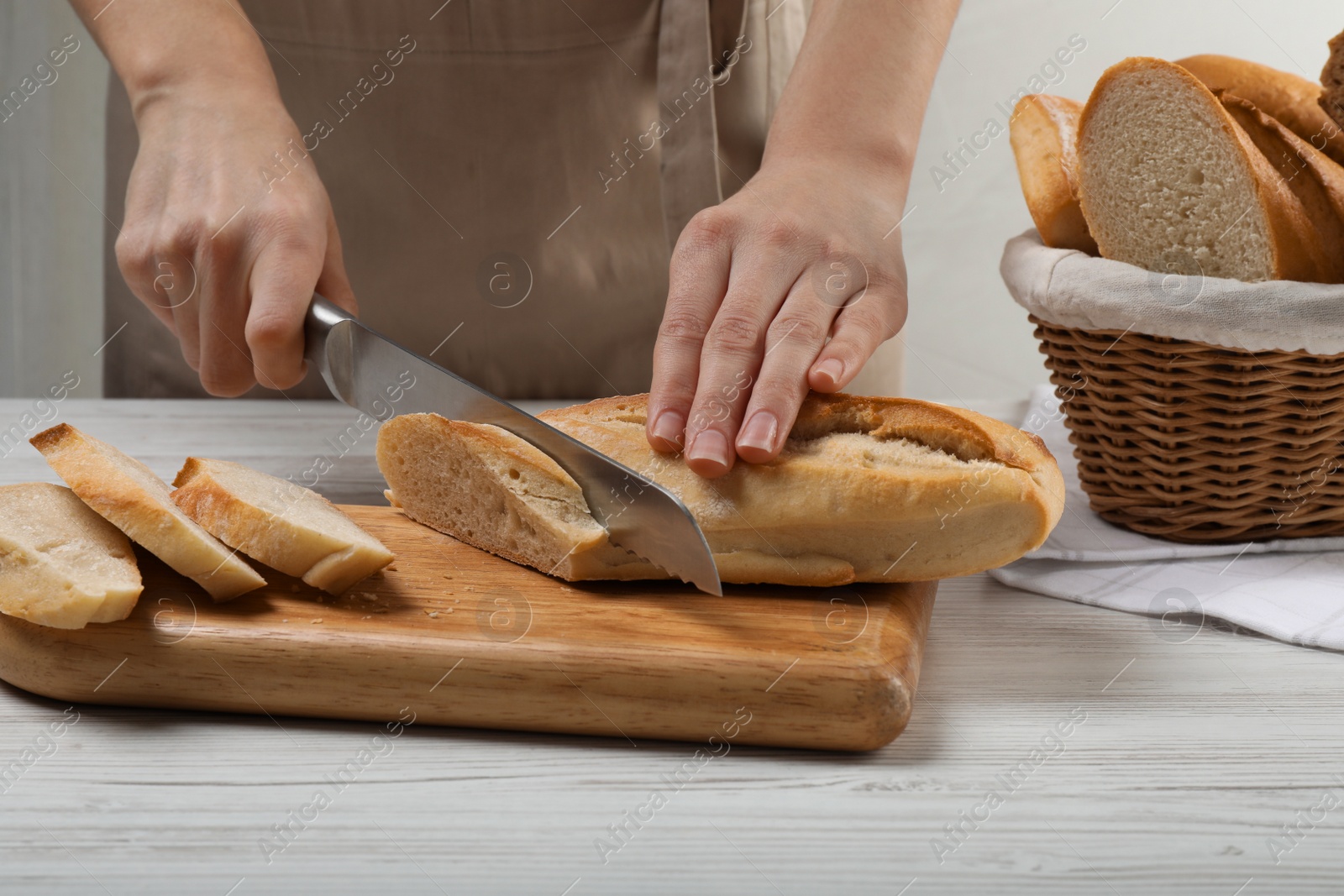 Photo of Woman cutting freshly baked baguette at white wooden table, closeup