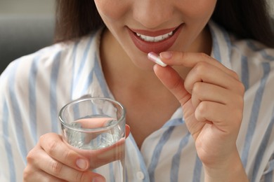 Photo of Young woman with glass of water taking dietary supplement pill, closeup