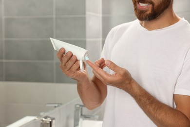 Photo of Handsome man applying cream in bathroom, closeup