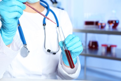 Photo of Laboratory worker pipetting blood sample into test tube for analysis, closeup