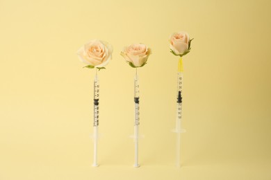 Photo of Medical syringes and rose flowers on pale yellow background
