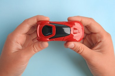 Photo of Child holding toy car on light blue background, top view