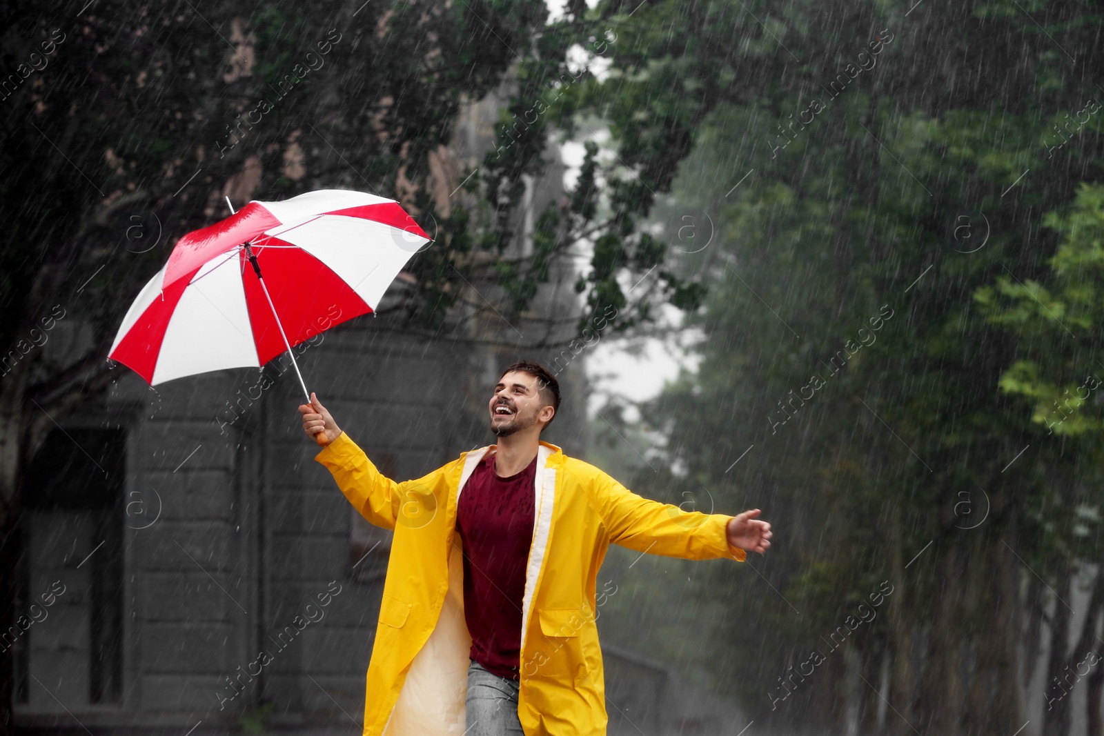 Photo of Happy young man with colorful umbrella outdoors on rainy day