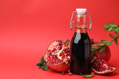 Photo of Tasty pomegranate sauce in bottle, branches and fruits on red background, closeup. Space for text