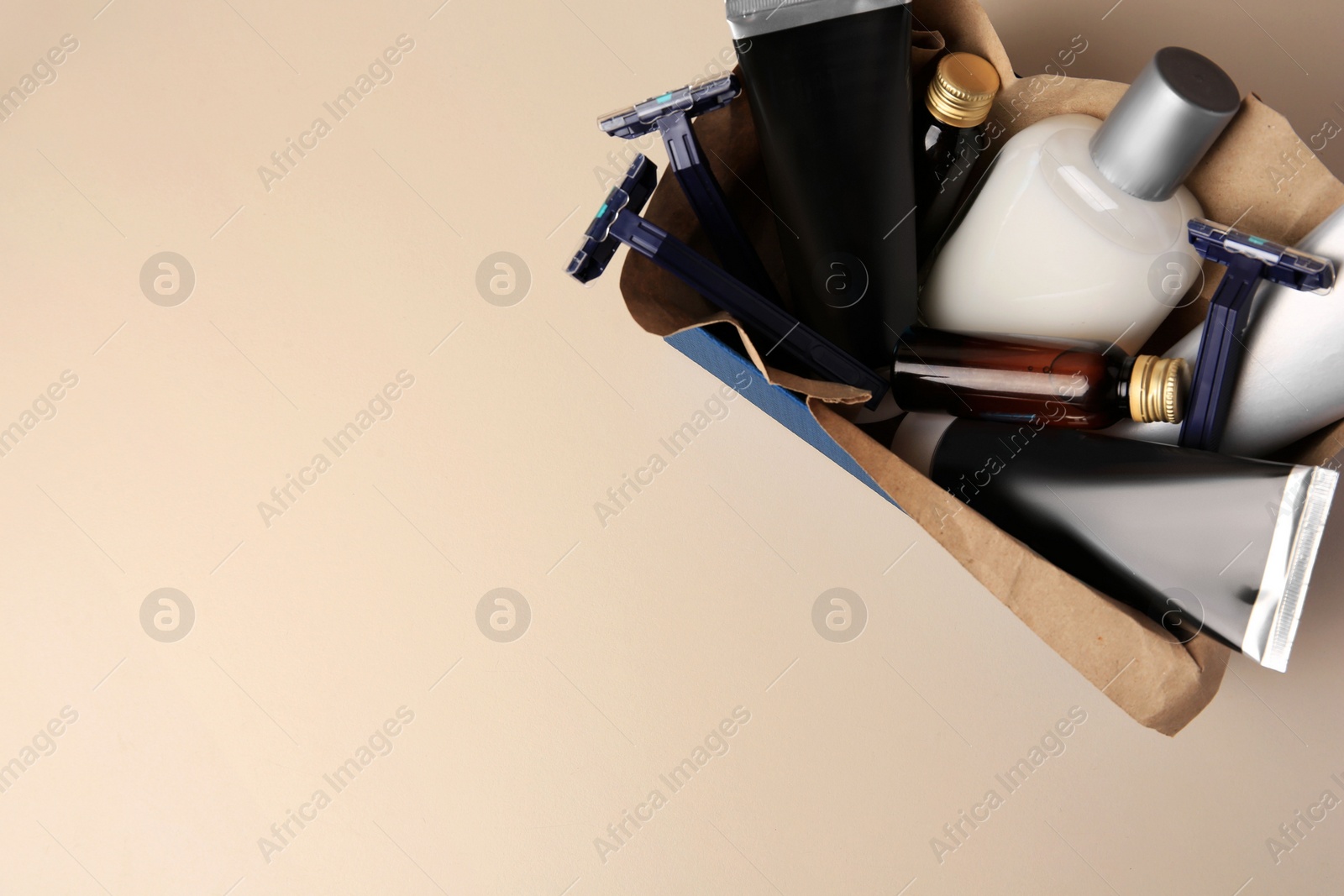 Photo of Box with different men's shaving accessories and cosmetics on beige background, top view. Space for text