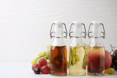 Photo of Different types of vinegar and ingredients on light tiled table, closeup. Space for text