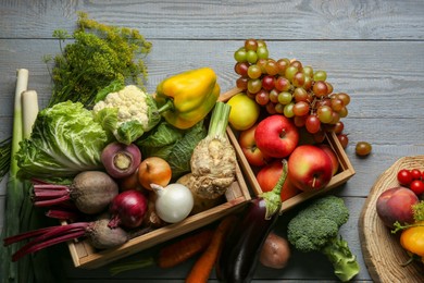 Photo of Different fresh vegetables and fruits in crates on grey wooden table, flat lay. Farmer harvesting
