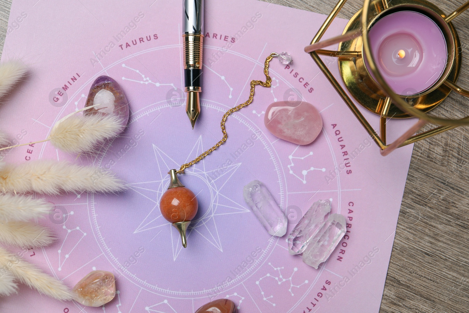 Photo of Astrology prediction. Zodiac wheel, gemstones, pendulum and burning candle on wooden table, flat lay