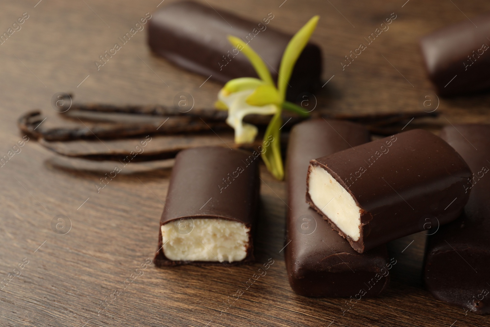 Photo of Glazed curd cheese bars, vanilla pods and flower on wooden table, closeup