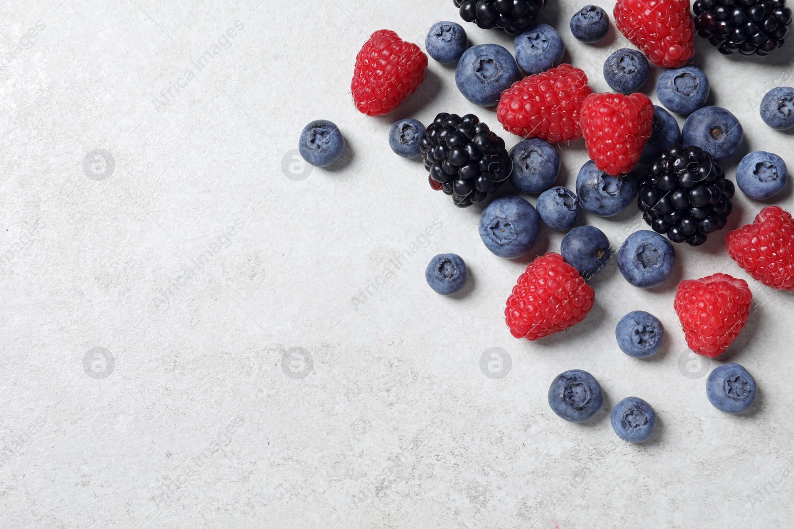 Photo of Many different fresh ripe berries on white textured table, flat lay. Space for text