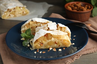 Photo of Delicious apple strudel with almonds, powdered sugar and mint on wooden table