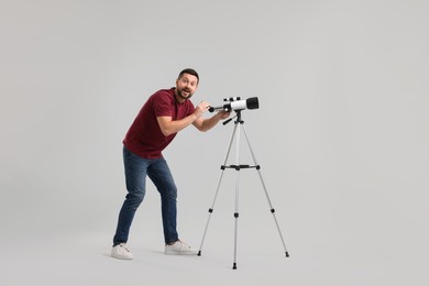 Happy astronomer with telescope on light grey background