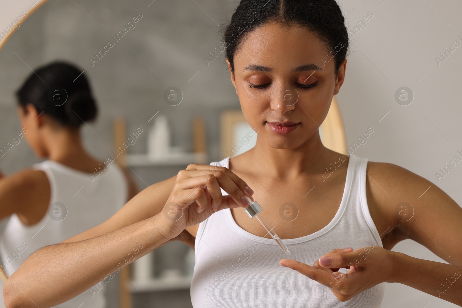 Photo of Beautiful woman applying serum onto her finger in bathroom
